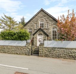 Exterior view of a stone house with arched windows and a gate in front at Horeb Chapel House in Tanygrisiau