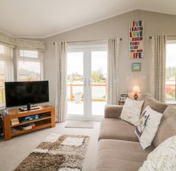 A living room with a sofa a TV on a stand and a rug at Lake View Lodge in Marston near Barkston