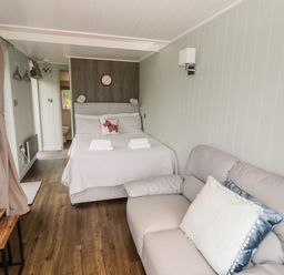 A bedroom with a bed a sofa a clock flowers on a table and a bathroom visible at Hydrangea in Bretforton
