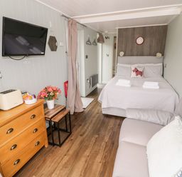 A bedroom with a bed sofa wooden dresser kettle toaster wall mounted TV and flowers at Hydrangea Bretforton