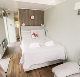 A bedroom with a bed with white linens and towels a chair and a bathroom visible at Hydrangea in Bretforton