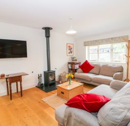 A living room with two sofas red pillows a wood stove a wall-mounted tv and a window at Shippon Barn in Yeovil