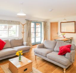A living room with two grey sofas with red cushions a wooden coffee table with flowers and a dining table with chairs at Shippon Barn in Yeovil