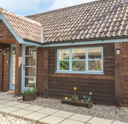 The exterior of a building with wooden cladding blue framed windows a tiled roof and flower planters on a gravel ground at Shippon Barn in Yeovil