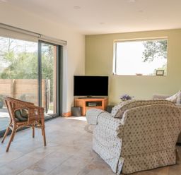 A living room with a wicker chair a patterned armchair a beige sofa and a corner TV at Black Cat Bach in Gilwern