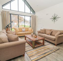 A living room with two brown sofas a yellow sofa a wooden coffee table and a telescope near a large window at Lambs Lodge in Bamburgh