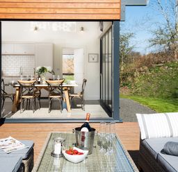 An outdoor seating area with a table holding a wine bottle in a cooler glasses and a bowl of strawberries with a dining area visible through open glass doors at Lambs Lodge in Bamburgh