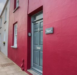 A row of colorful houses along a sidewalk with a blue door and a sign that says Bari in Aberaeron