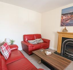 A living room with red leather sofas a wooden coffee table and a fireplace with a painting above at Bari Aberaeron