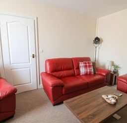 A living room with red leather sofas a wooden coffee table and a white door at Bari in Aberaeron