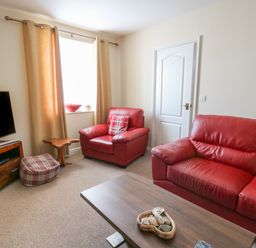 A living room with red leather sofas a wooden coffee table a TV on a stand and beige curtains at Bari in Aberaeron