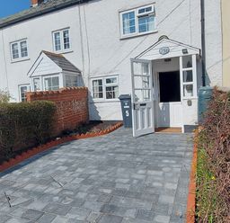 A white house with an open door a paved driveway and trimmed hedges at Meadow View Cottage in Lympstone