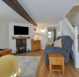 A living room with a gray sofa wooden tables a fireplace wall-mounted TV and a staircase at Meadow View Cottage in Lympstone