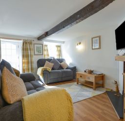 A living room with gray sofas and yellow cushions a wooden coffee table mounted TV and wooden furniture at Meadow View Cottage in Lympstone