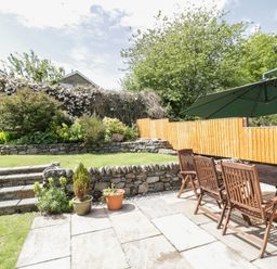 A garden with stone steps and walls wooden table and chairs with an umbrella and plants in pots at Clyd Fan in Harlech