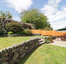 A garden with stone walls wooden fence outdoor dining table and umbrella at Clyd Fan in Harlech