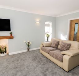 A living room with a beige sofa a wall-mounted TV and plants in Harlech
