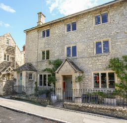 A stone house with multiple windows and a small fenced garden at The Old Post Office in Coln St Aldwyns