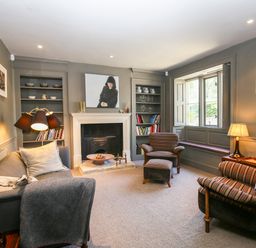 A living room with a fireplace two striped armchairs a gray sofa bookshelves and a window seat at The Old Post Office in Coln St Aldwyns