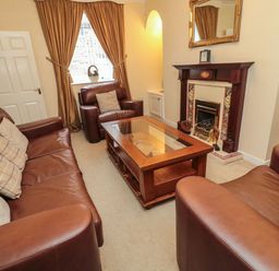 A living room with brown leather sofas a wooden coffee table and a fireplace at Victoria Cottage in Amble