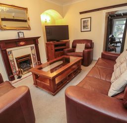 A living room with leather sofas a wooden coffee table a fireplace and a television at Victoria Cottage in Amble