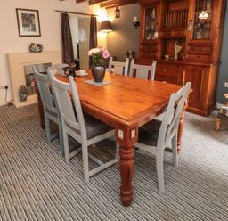 A dining room with a wooden table and six chairs a wooden cabinet and striped carpet at Victoria Cottage in Amble