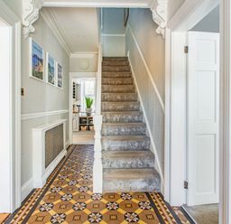 A hallway with patterned tiled floor leading to carpeted stairs and doors to adjacent rooms at Bryn Rhosyn in Nefyn