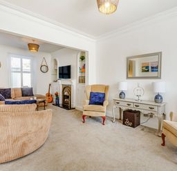 A living room with beige sofas a TV on a white cabinet and a console table with two lamps at Bryn Rhosyn in Nefyn