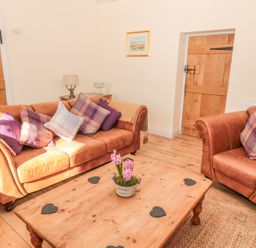 A living room with brown leather sofa and armchair pillows wooden coffee table and wooden doors at Baytree in Alnwick