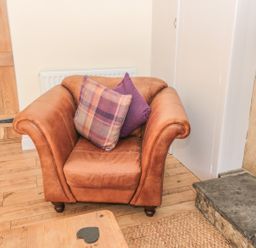 A brown leather armchair with two cushions in a room with wooden flooring and a stone fireplace at Baytree in Alnwick