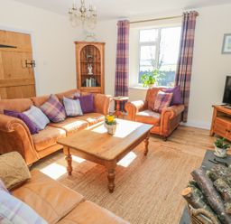 A living room with leather sofas a wooden coffee table a television and a wood-burning stove at Appletree in Alnwick