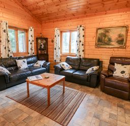 A living room with two black leather sofas a brown leather armchair wooden coffee table striped rug wood paneled walls and two windows at Chloes Lodge in Middleton Ryedale