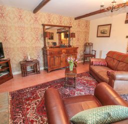 A living room with leather armchairs a sofa a wooden cabinet a television and a red patterned rug at Holly Cottage in Alnwick