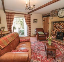 A living room with leather sofas a wooden coffee table and a fireplace with stacked logs at Holly Cottage in Alnwick