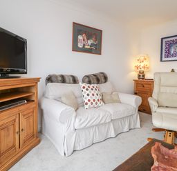 A living room with a sofa and armchair a television on a wooden cabinet and artwork on the walls at 14 Lyme Mews in Seaton Devon