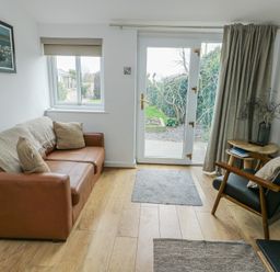 A living room with a sofa and door leading to the garden at Bwthyn in Moelfre