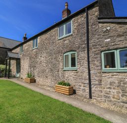 An outdoor view of a stone house with flower beds at Dale Barton in Wells