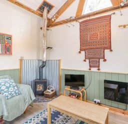 A living room with a wood stove a plaid armchair a coffee table a small tv and decorative wall hangings at Little Willow in Farrington near Child Okeford