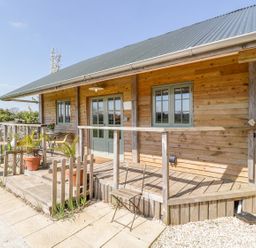 A wooden cabin with a green roof and a small porch with potted plants a chair and a wooden fence at Little Willow in Farrington near Child Okeford