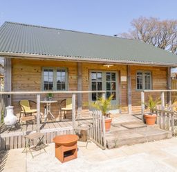 A wooden cabin with a green metal roof and a small porch with chairs and plants at Little Willow in Farrington near Child Okeford
