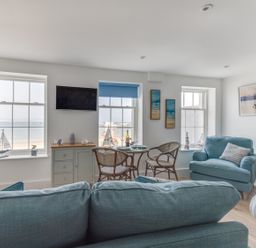 A living room with blue sofas a dining table with chairs and windows overlooking the sea at 6 The Beaches in Weymouth