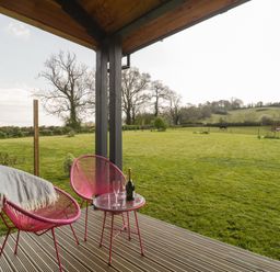 A covered patio with two pink chairs and a small table overlooking a grassy field at Bluebell in Sticklinch West Pennard Glastonbury