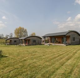 Three wooden cabins with curved roofs on a grassy field under a partly cloudy sky at Bluebell in Sticklinch West Pennard Glastonbury