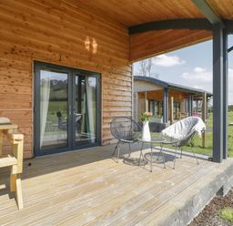 A covered wooden patio with black metal chairs and a small round table with flowers at Primrose in Sticklinch West Pennard Glastonbury