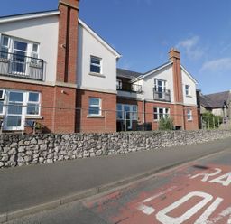 A two story brick and white house with balconies and a stone wall in front and a road with RAF LON marking