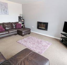 A living room with brown leather sofas a purple rug a wall-mounted fireplace and a television on a glass stand at Bay View in Benllech