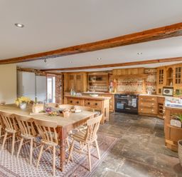 A kitchen and dining area with a long wooden table and chairs a kitchen island and wooden cabinets at Manor Farm Barn Dewlish