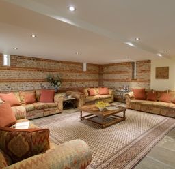 A sitting room with patterned sofas and red cushions around a wooden coffee table on a large rug at Manor Farm Barn in Dewlish