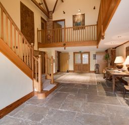 A hallway with a wooden staircase stone floor a rug wooden table with lamps and chairs at Manor Farm Barn in Dewlish
