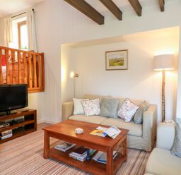 A living room with sofas a wooden coffee table a television and wooden staircase at Woodstock Cottage in Birchill near Chardstock